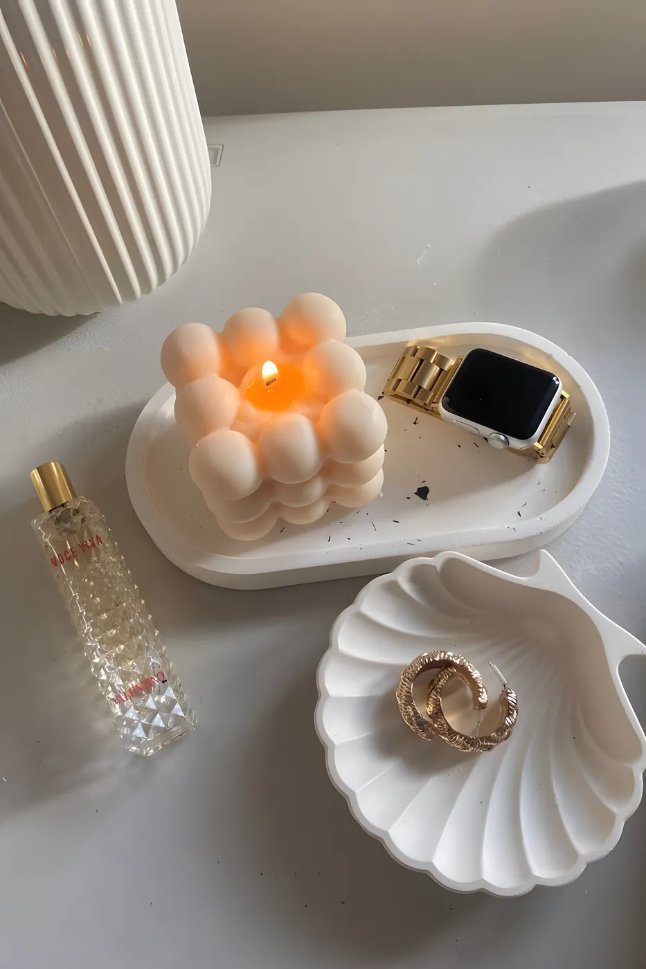 A lit Bubble Bliss candle on an oval concrete tray beside a shell tray holding rings